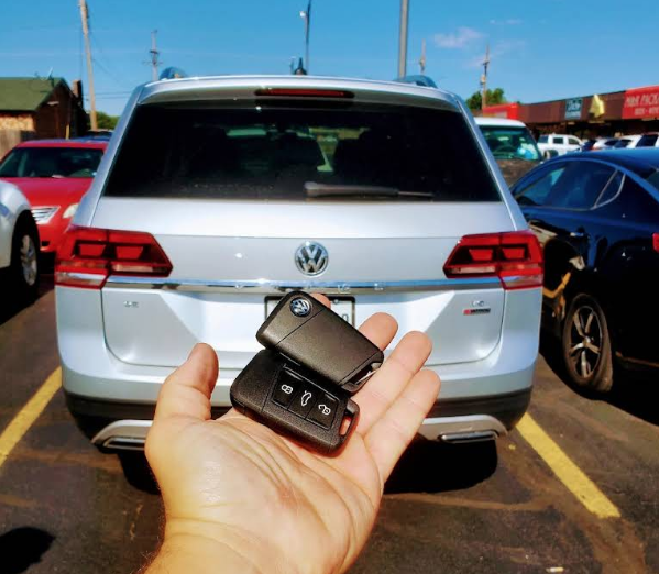 A hand holds up a pair of key fobs in front of a Volkswagen Atlas, the hands conveniently cover the license plate on the vehicle.