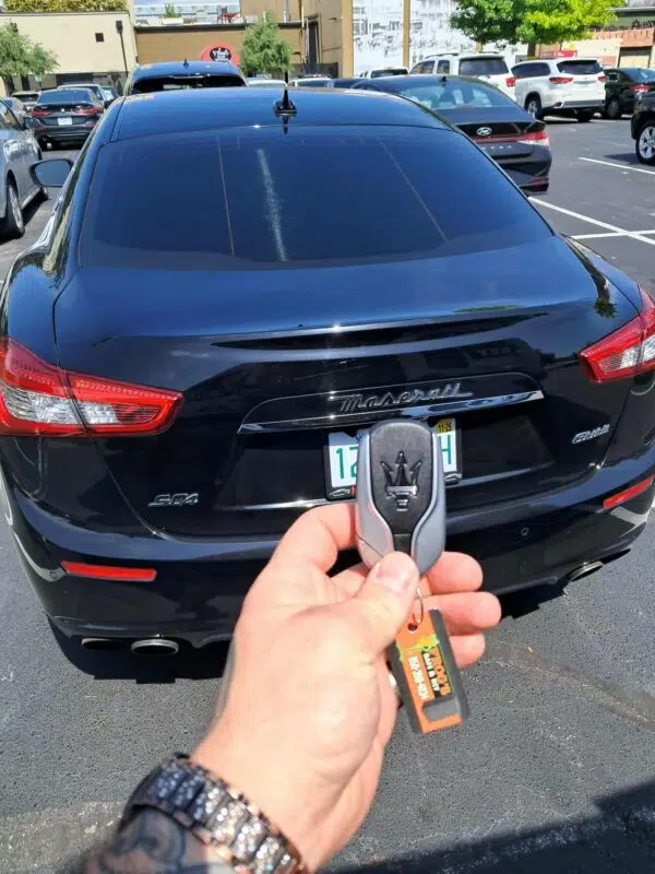 A hand holding a newly-programmed key fob for a Maserati S04 in front of the car.